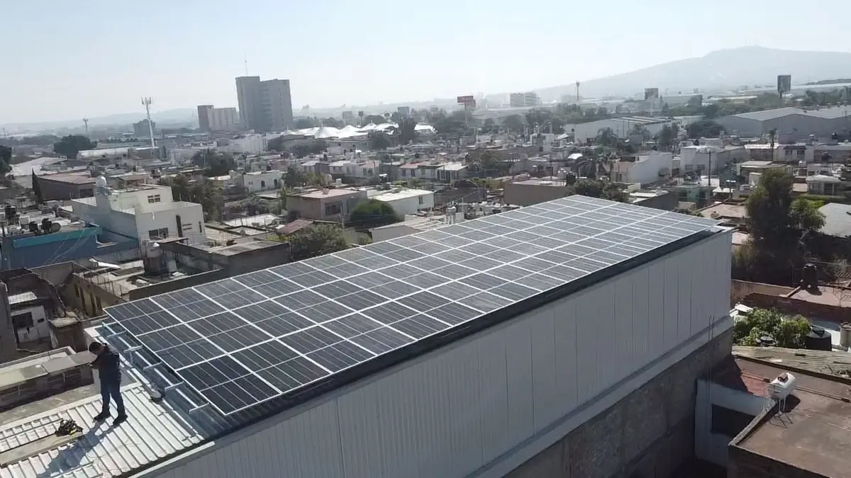 Instalación solar industrial en techo de lámina, toma aérea con la ciudad al fondo